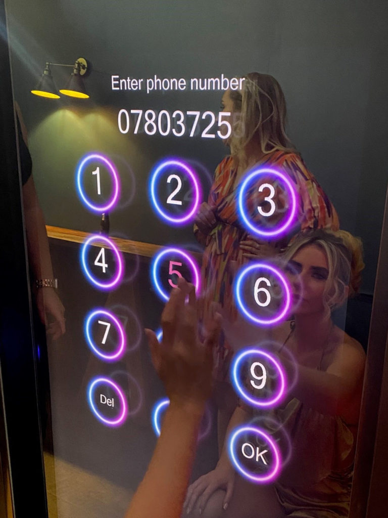 A guest tapping the illuminated on-screen keypad of a photo booth to have their photo sent to their phone