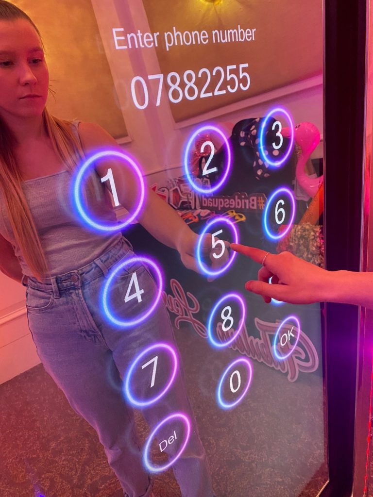 A guest entering their phone number on the illuminated keypad of a magic mirror photo booth